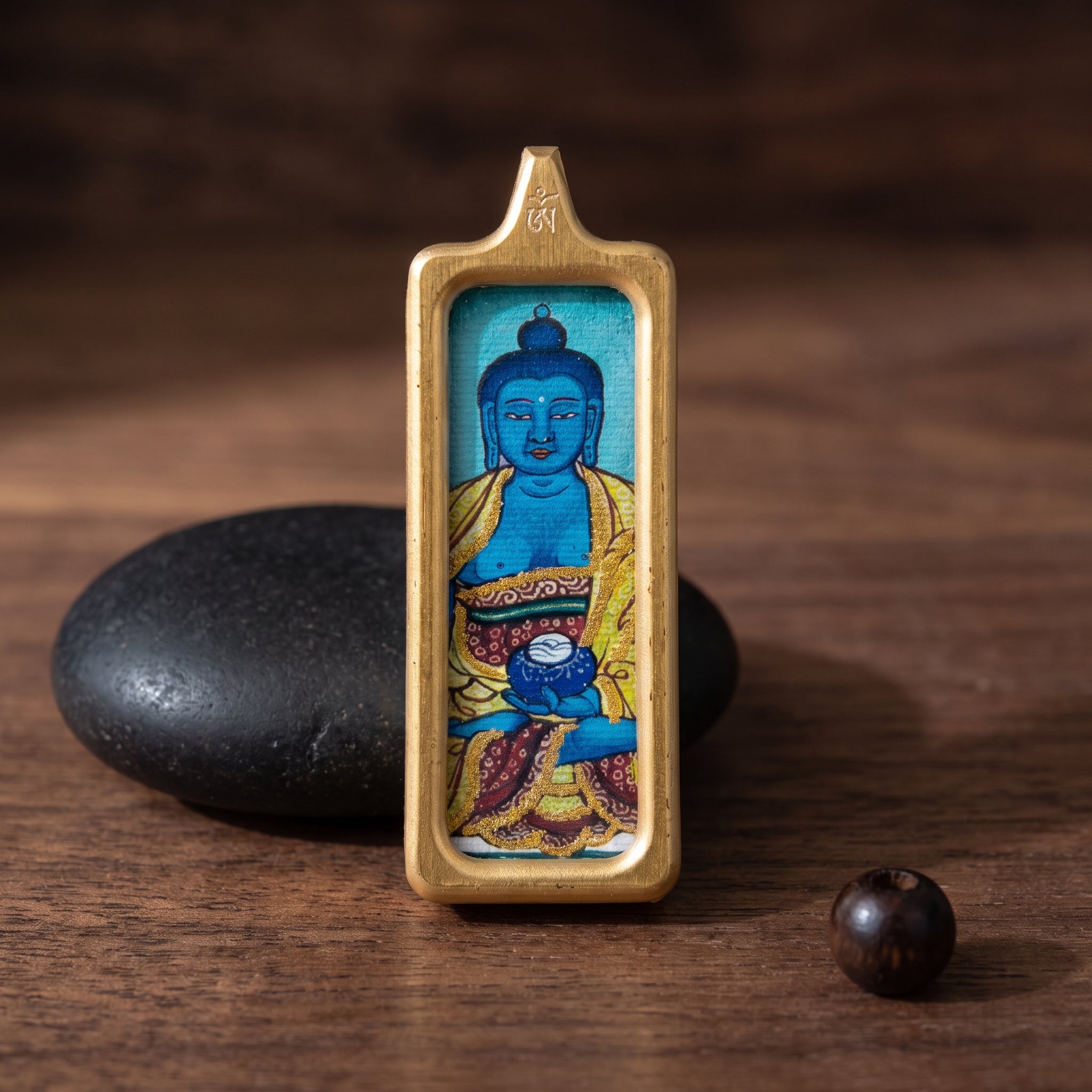 藥師佛長方形手繪描金佛牌情境展示圖，佛牌置於深色木面與黑石旁，呈現沉穩靜心氛圍。