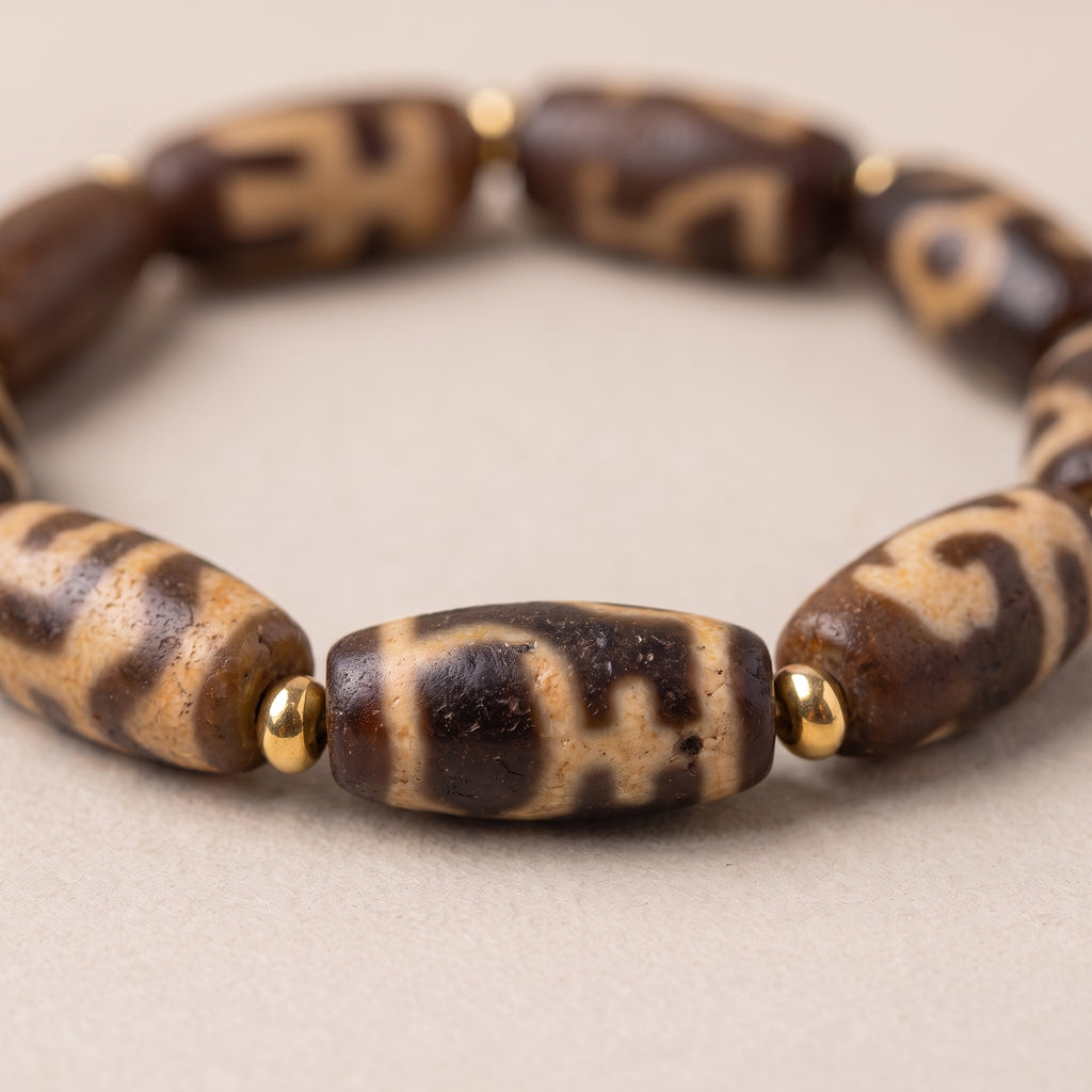Close-up of the weathered old dzi bead bracelet showing the aged bead texture, pattern details, and gold spacer beads.