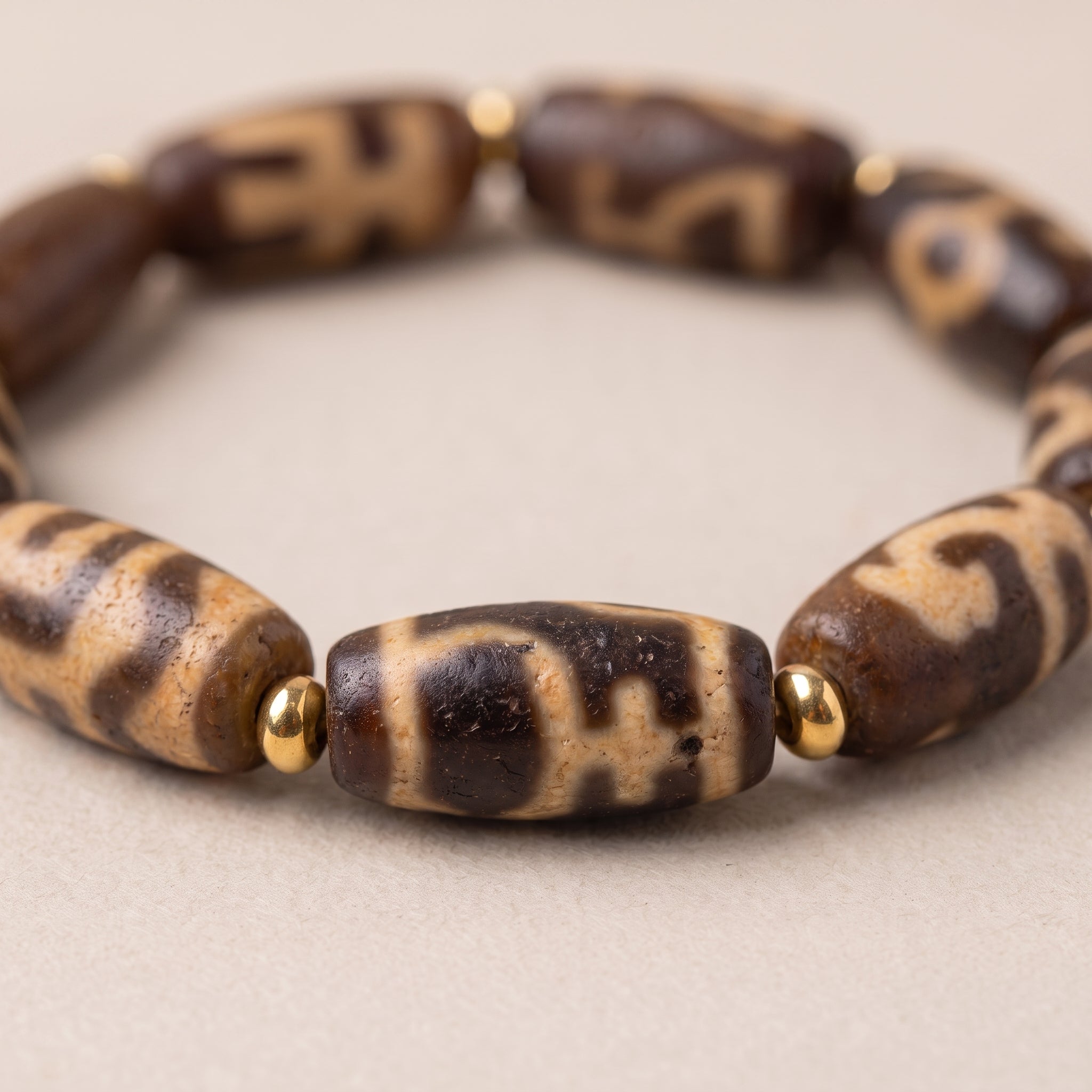 Close-up of the weathered old dzi bead bracelet showing the aged bead texture, pattern details, and gold spacer beads.
