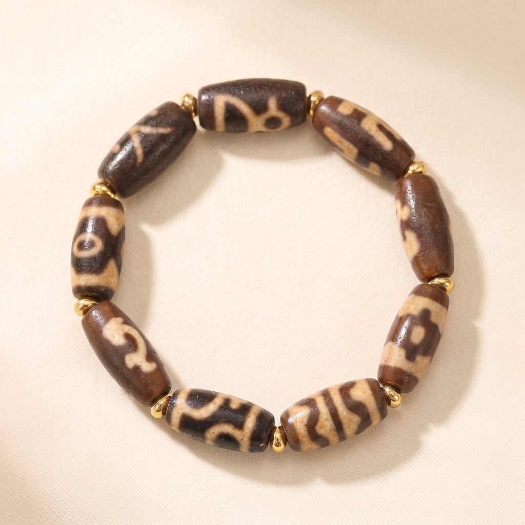 Weathered old dzi bead bracelet with 9 patterned beads and gold spacers on a light neutral background.