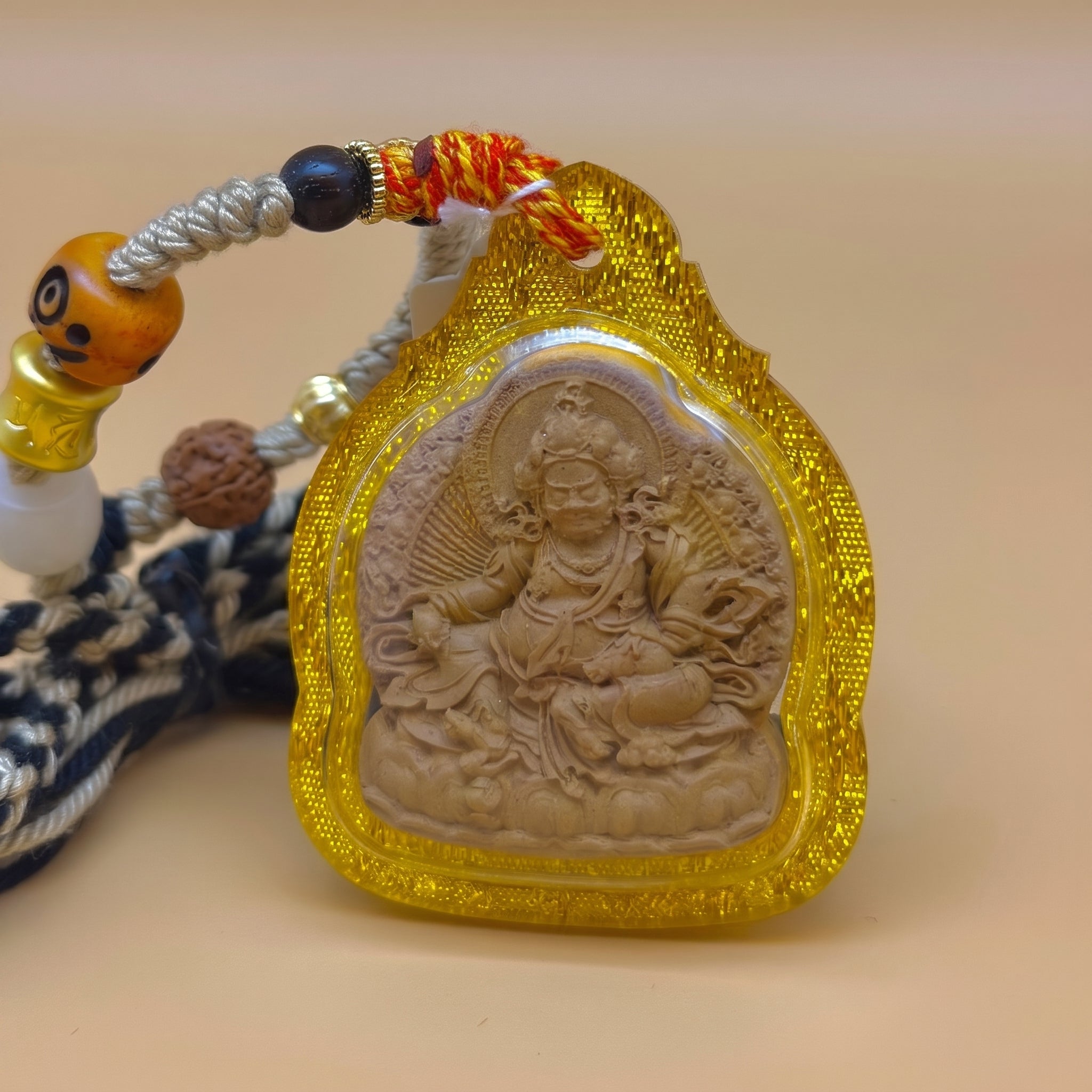 黃財神佛牌擦擦牌內藏法米正面圖，展示透明黃色護殼、泥塑浮雕黃財神法相、編繩及珠飾配件